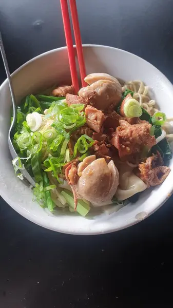 A mouthwatering bowl of Asian culinary delight featuring savory leeks and succulent meatballs, accompanied by chopsticks, resting on a well-set table