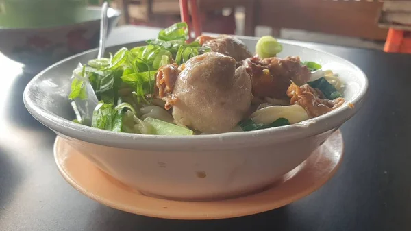 A mouthwatering bowl of Asian culinary delight featuring savory leeks and succulent meatballs, accompanied by chopsticks, resting on a well-set table