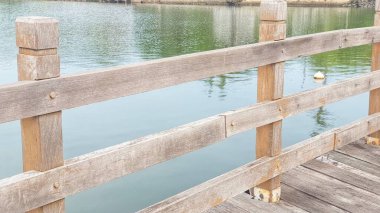 Sakin bir su arka planına kurulmuş, yıpranmış tahtaları ve korkulukları olan ahşap bir rıhtım manzarası. Doğa, açık hava yapıları ve sakin manzaralar ile ilgili konular için ideal