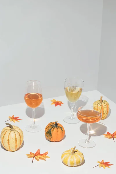 Gri arka planda çeşitli doğal renkli balkabaklarıyla yaratıcı sonbahar sahnesi, bir bardak içki ve sonbahar yaprakları. Sonbahar tatili ya da parti konsepti.
