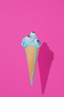 Gözleri ve erimiş mavi dondurması olan dondurma külahı. Ürkütücü Cadılar Bayramı konsepti. Canlı renkler arkaplanı.