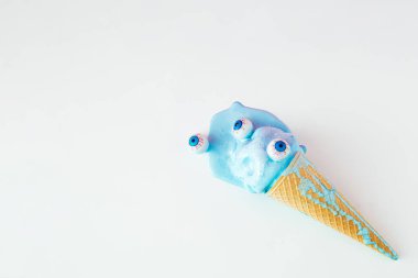 Gözleri ve erimiş mavi dondurması olan dondurma külahı. Ürkütücü Cadılar Bayramı konsepti. Canlı renkler arkaplanı.