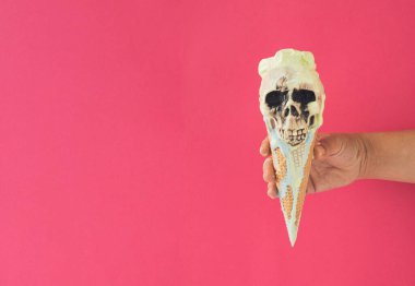 Elinde kafatası olan dondurma külahı, eriyen mavi ve yeşil dondurma. Ürkütücü Cadılar Bayramı konsepti. Canlı renkler arkaplanı.