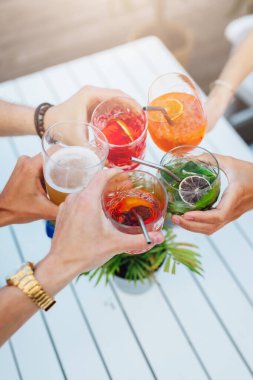 Bir grup arkadaş yaz terasında rengarenk kokteyllere kadeh kaldırıyor.  