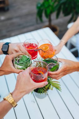 Bir grup arkadaş yaz terasında rengarenk kokteyllere kadeh kaldırıyor.  