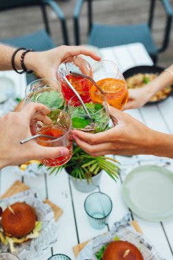 Bir grup arkadaş yaz terasında rengarenk kokteyllere kadeh kaldırıyor.  
