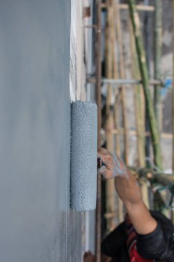 Duvarı boyamak için boya silindiri kullanıyor.