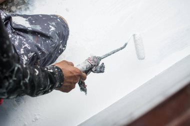 Duvarı boyamak için boya silindiri kullanıyor.