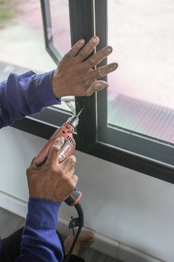 Çelik çerçevede elektrikli tornavida kullanan bir adam.