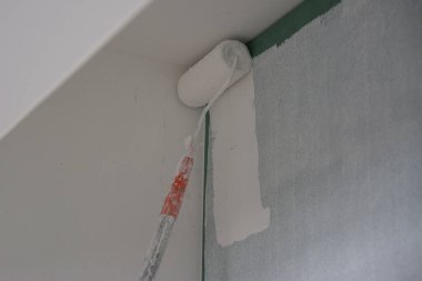 Duvarı boyamak için boya silindiri kullanıyor.