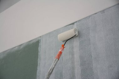 Duvarı boyamak için boya silindiri kullanıyor.