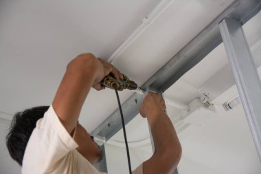 Adam kare çeliği delmek için elektrikli matkap kullanıyor.