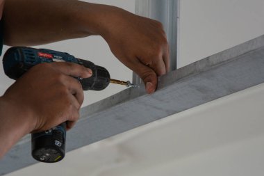 Adam kare çeliği delmek için elektrikli matkap kullanıyor.