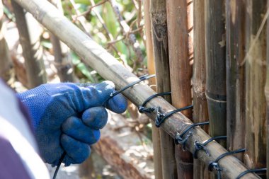İşçi, zincirli tel örgüyü örtmek için alüminyum tel ile birbirine bağlanmış bambu duvar panelleri kurar.