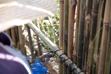 İşçi, zincirli tel örgüyü örtmek için alüminyum tel ile birbirine bağlanmış bambu duvar panelleri kurar.