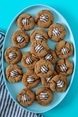 Gingerbread blossom holiday cookies, with white chocolate striped candy on blue oval plate with gray striped napkins on left side