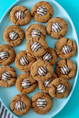 Close up of stack of gingerbread blossom holiday cookies, with white chocolate striped candy on blue oval plate with gray striped napkins on left side