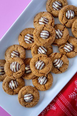 Gingerbread blossom cookies, with white chocolate striped candy stacked on white plate with red and white snowflake napkin on bottom