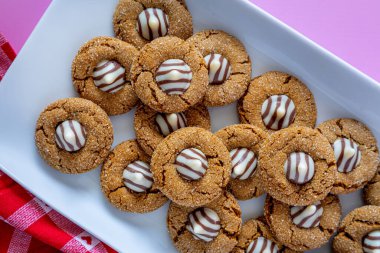 Close up of gingerbread blossom holiday cookies, stacked on white rectangle plate with red and white heart checked napkin on pink background
