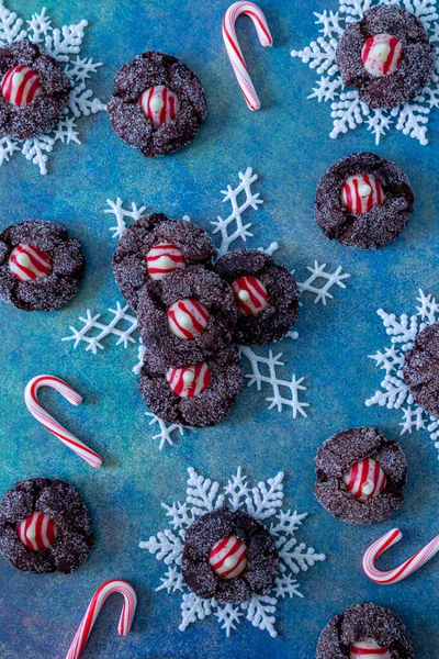 Close up of cookie display of candy cane chocolate blossom cookies on white glitter snowflakes with small candy canes, sitting on bright blue abstract background