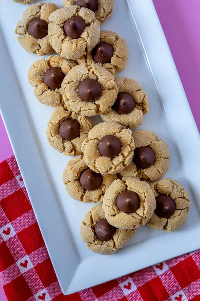 stock image Close up of plate of peanut butter blossom cookies, stacked on white rectangle plate with heart red and white checked napkin sitting on pink background