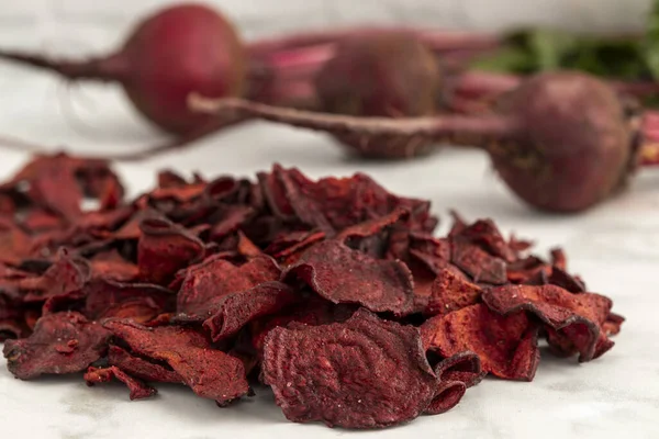Close up of red beet plant based chips with sea salt sitting in a pile on marble kitchen counter with fresh beet roots in the background