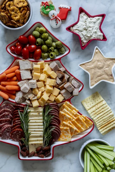 stock image Close up of holiday charcuterie display with Christmas tree shaped platter filled with meats, assorted cheese, vegetables and nuts with star shaped bowls filled with dips and additional snacks and vegetables. Vertical orientation.