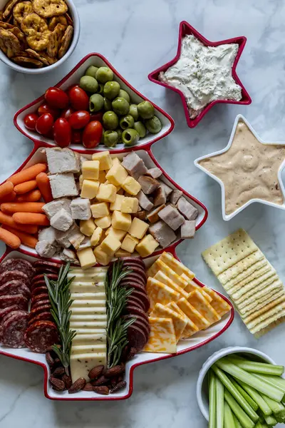 在红白相间的圣诞树形盘子里 摆满了各种肉类 奶酪和蔬菜 周围都是蘸汁和额外的零食 纵向方向 图库图片