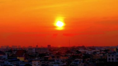 4K A time lapse of the large orange sunset as the massive sun sets into the horizon above the city