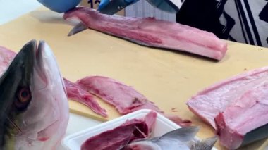 4K Şef ustalıkla Hamachi filetosu yapıyor. Balık kafası önünde görünüyor. Müşterilere servis yapmak için balığı kesme tahtasıyla kesiyor..