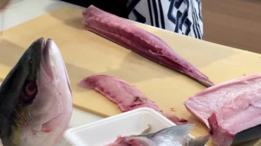 4K Şef ustalıkla Hamachi filetosu yapıyor. Balık kafası önünde görünüyor. Müşterilere servis yapmak için balığı kesme tahtasıyla kesiyor..