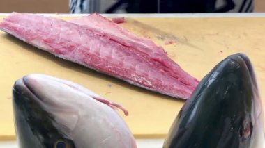 4K Şef ustalıkla Hamachi filetosu yapıyor. Balık kafası önünde görünüyor. Müşterilere servis yapmak için balığı kesme tahtasıyla kesiyor..