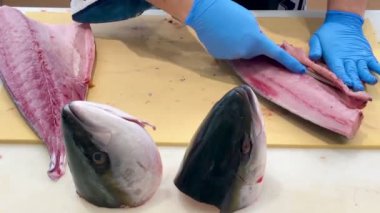 4K Şef ustalıkla Hamachi filetosu yapıyor. Balık kafası önünde görünüyor. Müşterilere servis yapmak için balığı kesme tahtasıyla kesiyor..