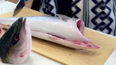 4K Şef ustalıkla Hamachi filetosu yapıyor. Balık kafası önünde görünüyor. Müşterilere servis yapmak için balığı kesme tahtasıyla kesiyor..