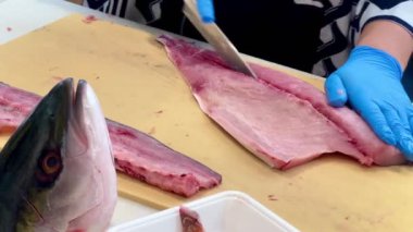 4K Şef ustalıkla Hamachi filetosu yapıyor. Balık kafası önünde görünüyor. Müşterilere servis yapmak için balığı kesme tahtasıyla kesiyor..