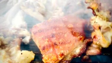 Domuz eti, kalın yağ ve küçük kömürleşmiş parçalarla kızartılıyor. Izgaradan duman yükseliyor, bu da etin kızgın kömürlerin ya da alevlerin üzerinde kızardığını gösteriyor. Et sulu görünüyor, sanki...