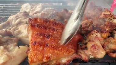 Domuz eti, kalın yağ ve küçük kömürleşmiş parçalarla kızartılıyor. Izgaradan duman yükseliyor, bu da etin kızgın kömürlerin ya da alevlerin üzerinde kızardığını gösteriyor. Et sulu görünüyor, sanki...