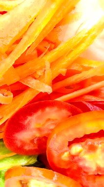 İnce dilimlenmiş havuç, kiraz domatesleri, dilimlenmiş kırmızı domates, yeşil (muhtemelen romaine marulu) ve dilimlenmiş sarı dolma biberli parlak ve taze bir salata. Dokuları çok farklı.