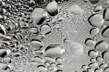 Metal yüzeydeki su damlacıklarının yoğunlaşmasını gösteren yüksek çözünürlüklü su damlalarının yakın çekim görüntüsü. Karmaşık desenler ve farklı boyutlardaki su damlacıkları güzel bir soyut doku oluşturur.. 