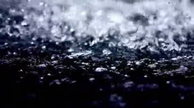 Düşen ve su damlacıklarını yüzeye sıçratan yakın çekim. Su damlacıkları havada donuyor, bazıları su yüzeyinden sekiyor ve bazıları küçük damlacıklara dönüşüyor..