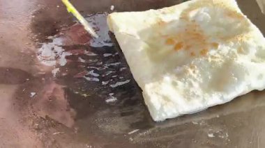 4k Street yiyecek satıcısı hamur ve tavada kızartılmış paratha roti 'yi dışarıda çıtır çıtır olana kadar kızgın yağda hazırlıyor. Sokak işportacısı sabah kahvaltısı için prata ekmeği veya roti canai hazırlıyor.