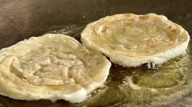 4k Street yiyecek satıcısı hamur ve tavada kızartılmış paratha roti 'yi dışarıda çıtır çıtır olana kadar kızgın yağda hazırlıyor. Sokak işportacısı sabah kahvaltısı için prata ekmeği veya roti canai hazırlıyor.