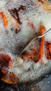  Şef kızgın yağda domuz kızartması yapıyor. En dikkat çekici nokta, metal bir spatula kullanarak kaynayan yağın yüzeyindeki altın-kahverengi domuz parçalarını kaldırmak. Bu da yüksek ısı ve cips olduğunu gösterir.