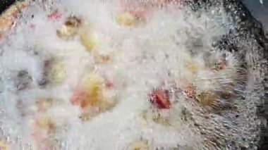  Şef kızgın yağda domuz kızartması yapıyor. En dikkat çekici nokta, metal bir spatula kullanarak kaynayan yağın yüzeyindeki altın-kahverengi domuz parçalarını kaldırmak. Bu da yüksek ısı ve cips olduğunu gösterir.