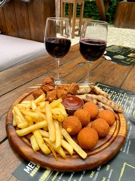 Dinner for two. Potatoes, nuggets, cheese balls and two glasses of red wine. An appetising dining table. A banner for the menu