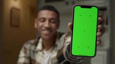 Adam hücrede dikey krom anahtarı gösteriyor. Elinde yeşil ekranlı cep telefonu olan Afro-Amerikalı bir adam. 4K
