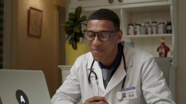 İnternetteki doktor dizüstü bilgisayara onay verdi. Keyifli Afrikalı Amerikalı pratisyen, klinikte dizüstü bilgisayarla konuşuyor. Çevrimiçi tıbbi danışmanlık. 4K