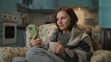 Evde görüntülü bir kadın var. 30 'lu yaşlardaki neşeli kadın internette rahat bir koltukta oturup sıcak çay içerek konuşuyor. 4K