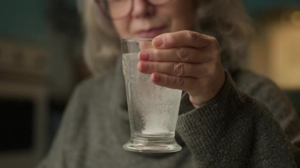 弾力性のある丸薬で水の高齢者の手保持ガラス 老人は家に座って薬を飲んでいる — ストック動画