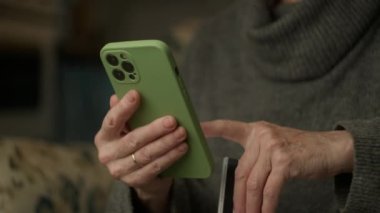 Yaşlı Eller Kredi Kartı ve Cep Telefonu ile Ödeme. Online ödeme için akıllı telefon kullanan tanınmamış yaşlı bir kadın. 4K
